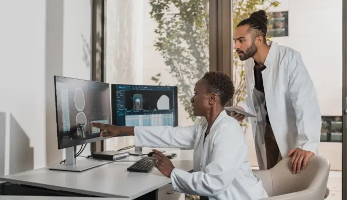 Two radiology professionals discussing patient information displayed on medical imaging results on a computer monitor in a bright office.