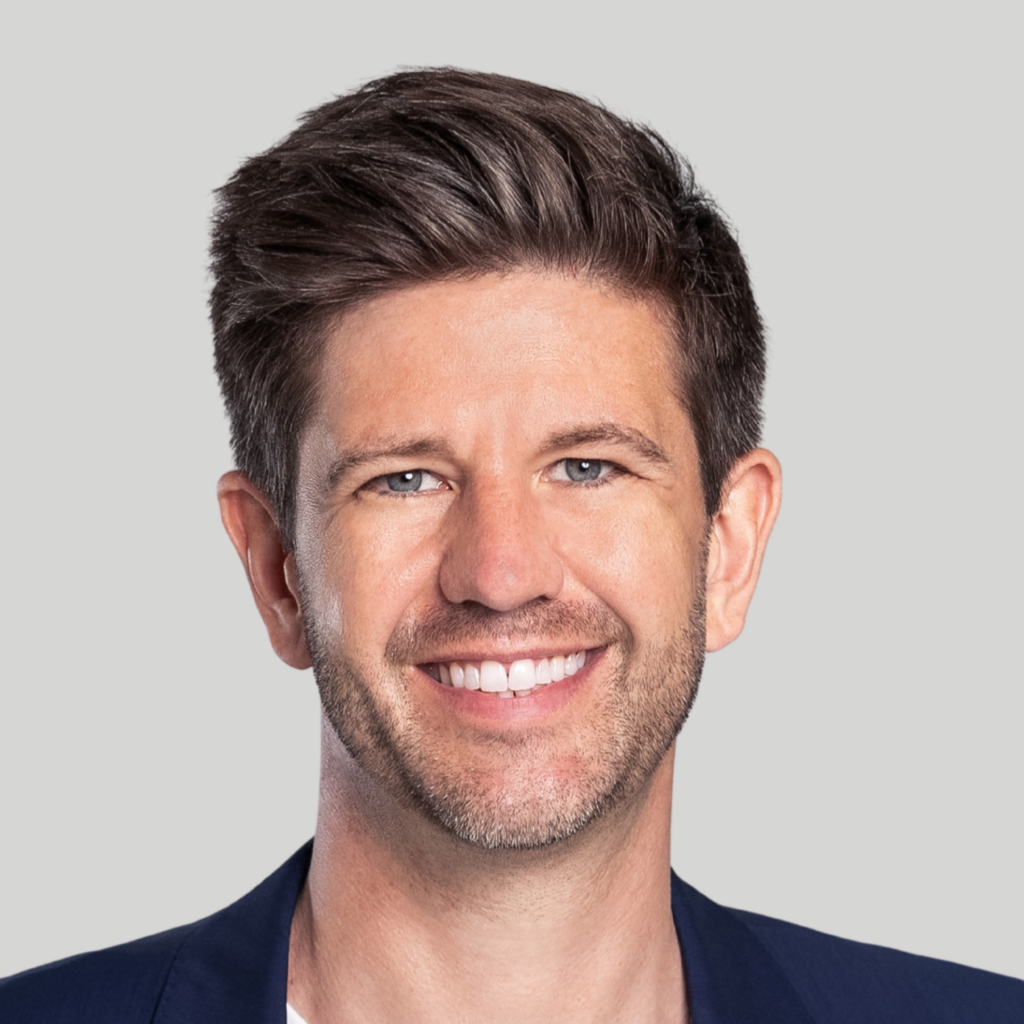 A man with short brown hair and a trimmed beard smiles at the camera, wearing a navy blazer and white shirt, ready to attend a Lunch and Learn at the upcoming RSNA 2026 event, against a light gray background.